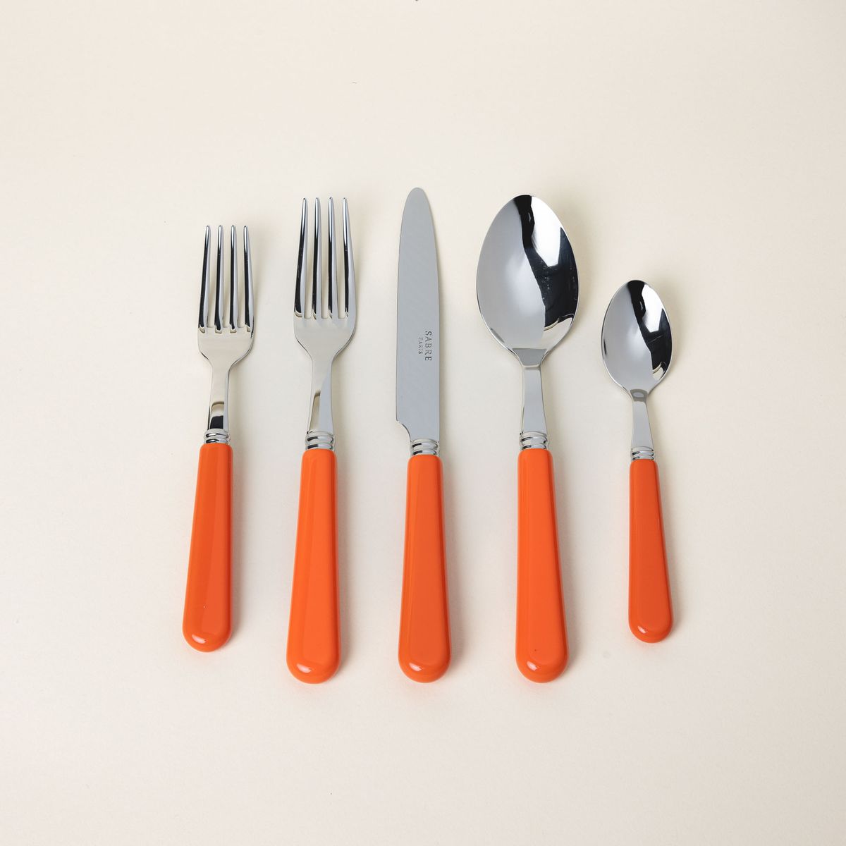 A five piece flatware set with shiny utensils and matte bold orange handles