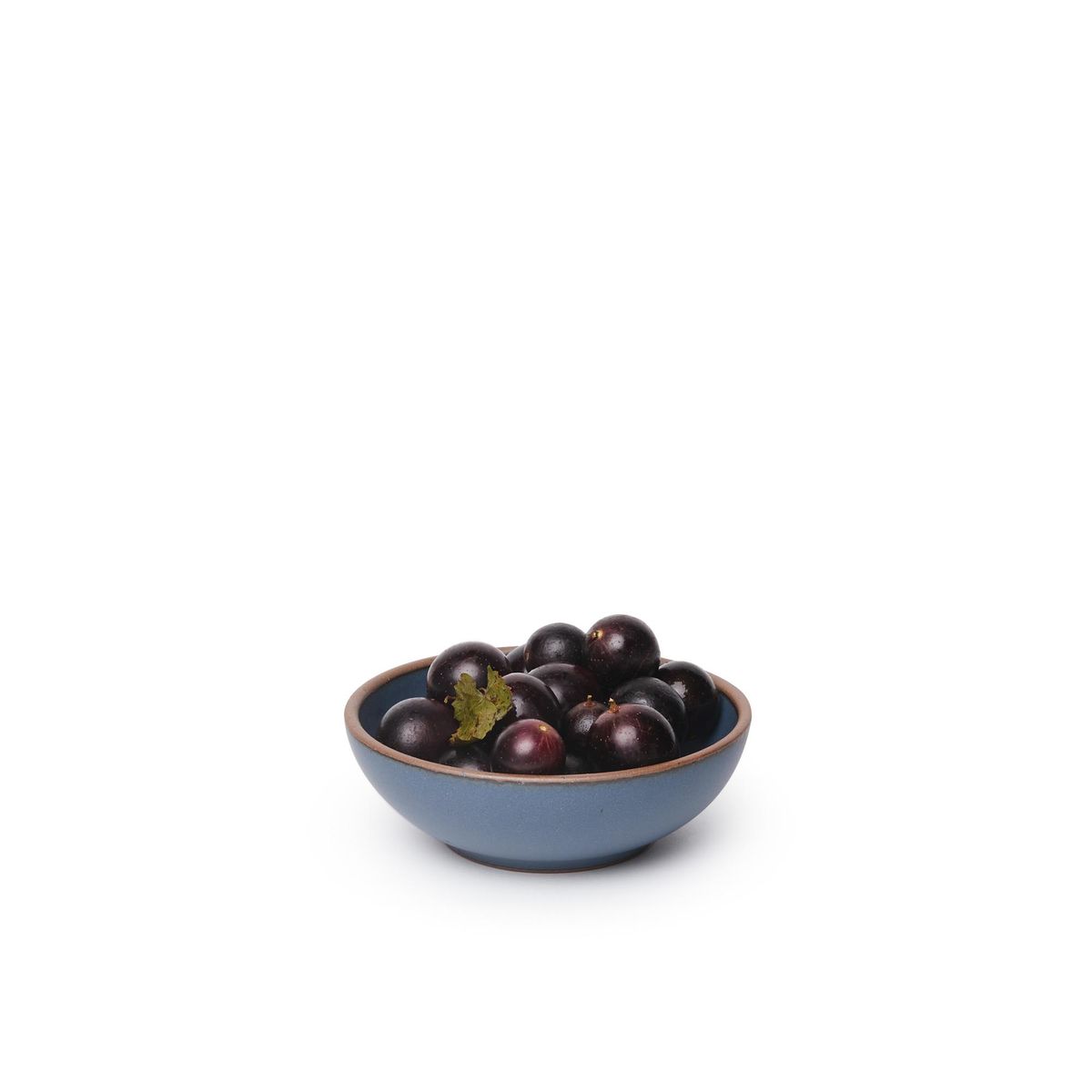 A small shallow ceramic bowl in a toned-down navy color featuring iron speckles and an unglazed rim, filled with cherries