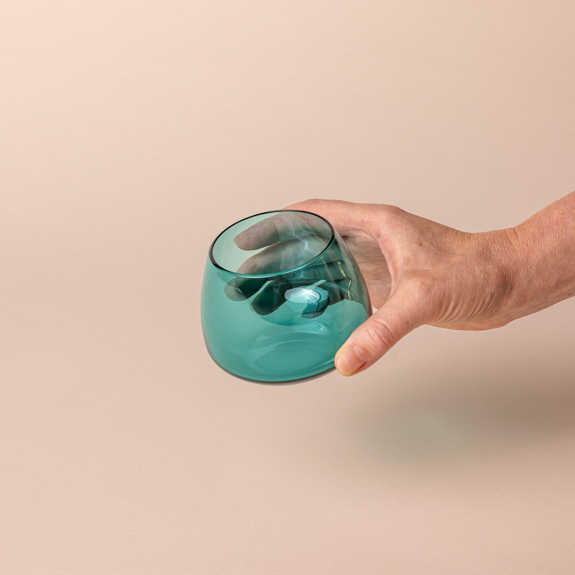 A hand holds a round short aqua blue glass punch cup with a round base that narrows a bit near the top.