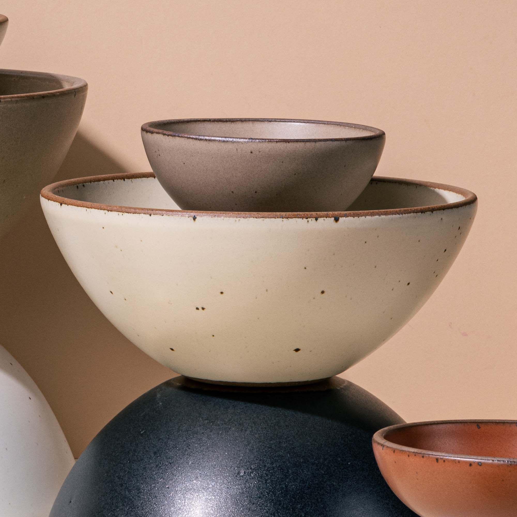 An artful arrangement of ceramic bowls with a focus on a popcorn bowl in an off-white color with iron speckles