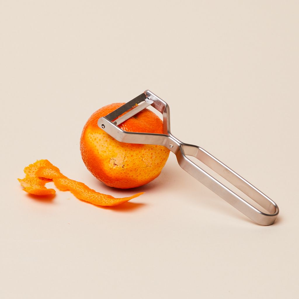 A stainless steel peeler's head rests atop a partially zested tangerine.