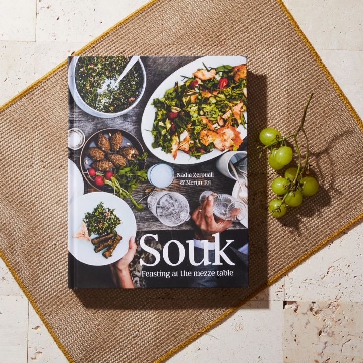 Book with the title "Souk" laying on a woven place next to green grapes