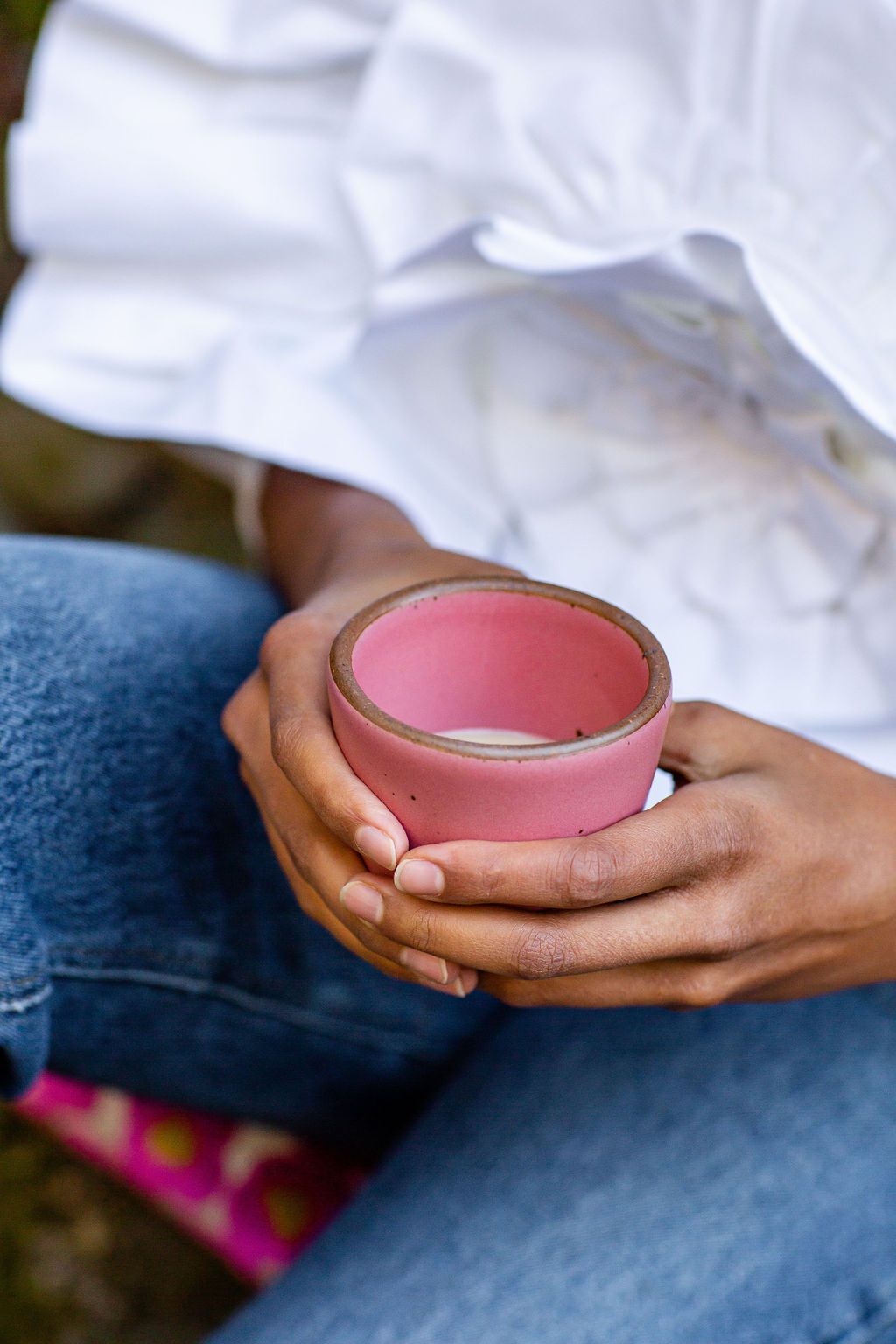 Two hands clasp around a hot pink cup filled with warm chai.