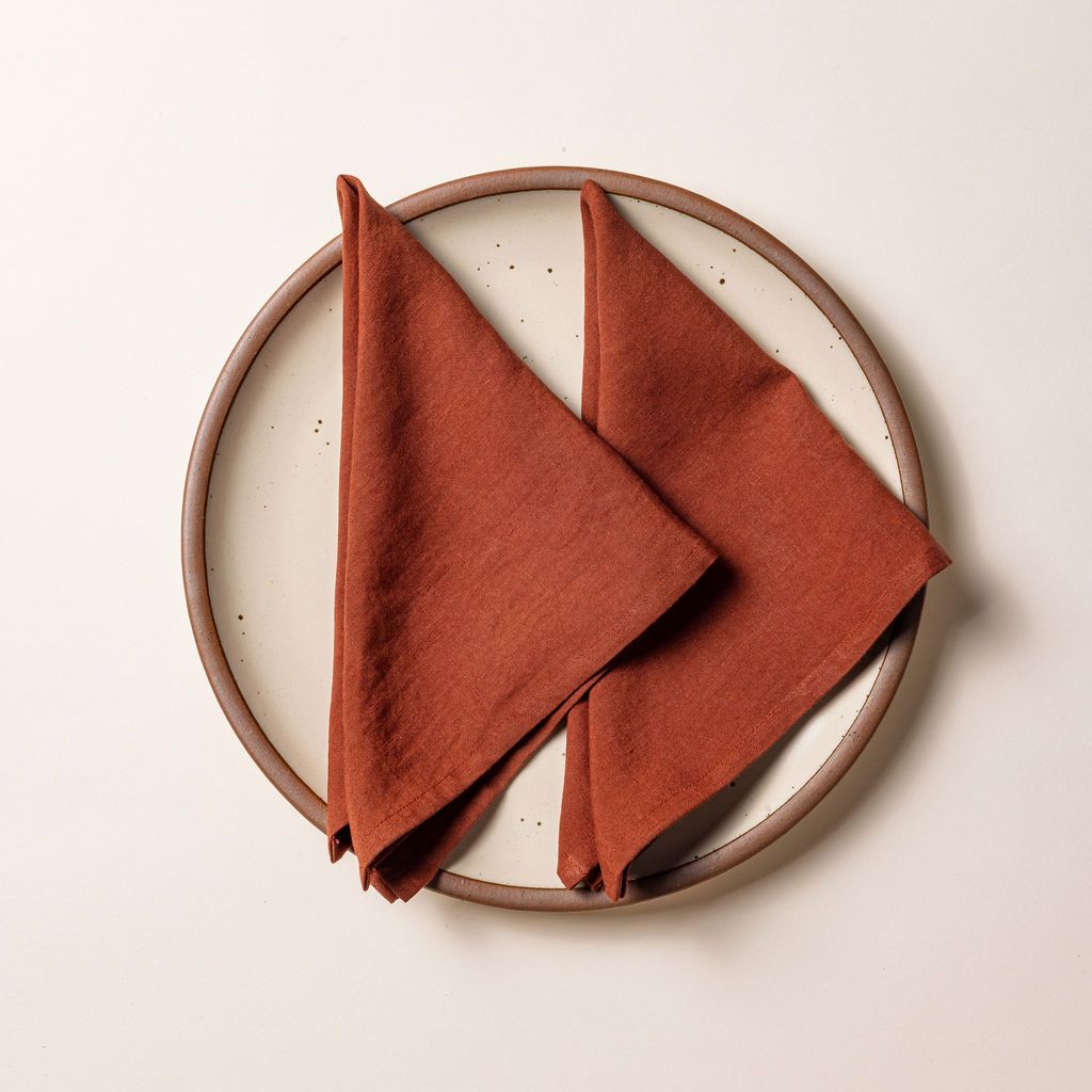 Two terracotta linen napkins folded into triangles on an off-white ceramic plate.