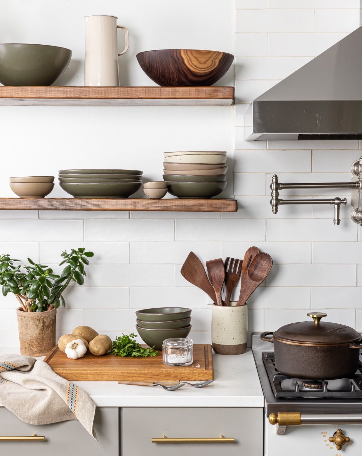 Open kitchen shelves filled with ceramic dinnerware, large wooden bowl, and a counter filled with kitchen utensils next to the oven.