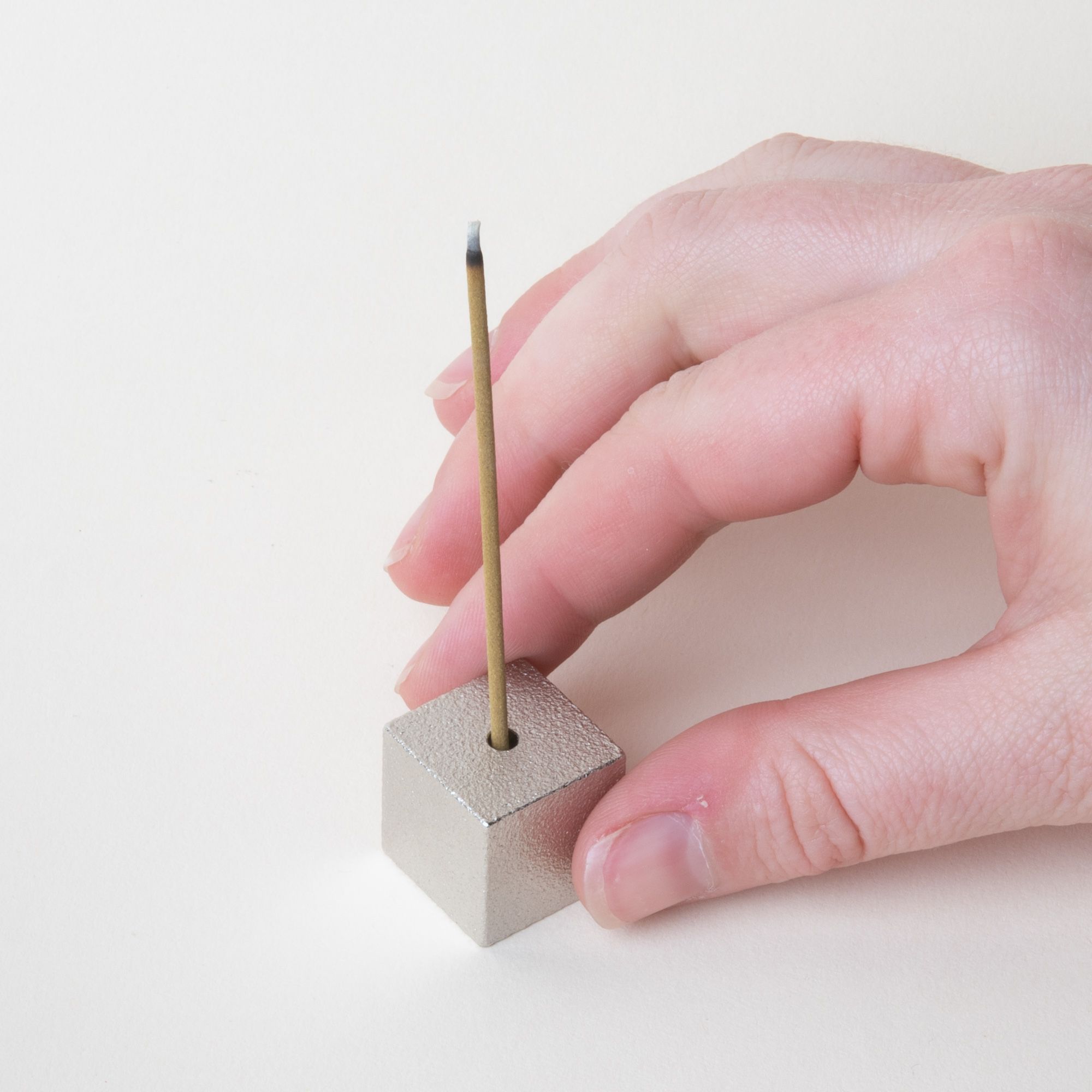 Hand holding a minimal cube made of pewter with incense sitting on top
