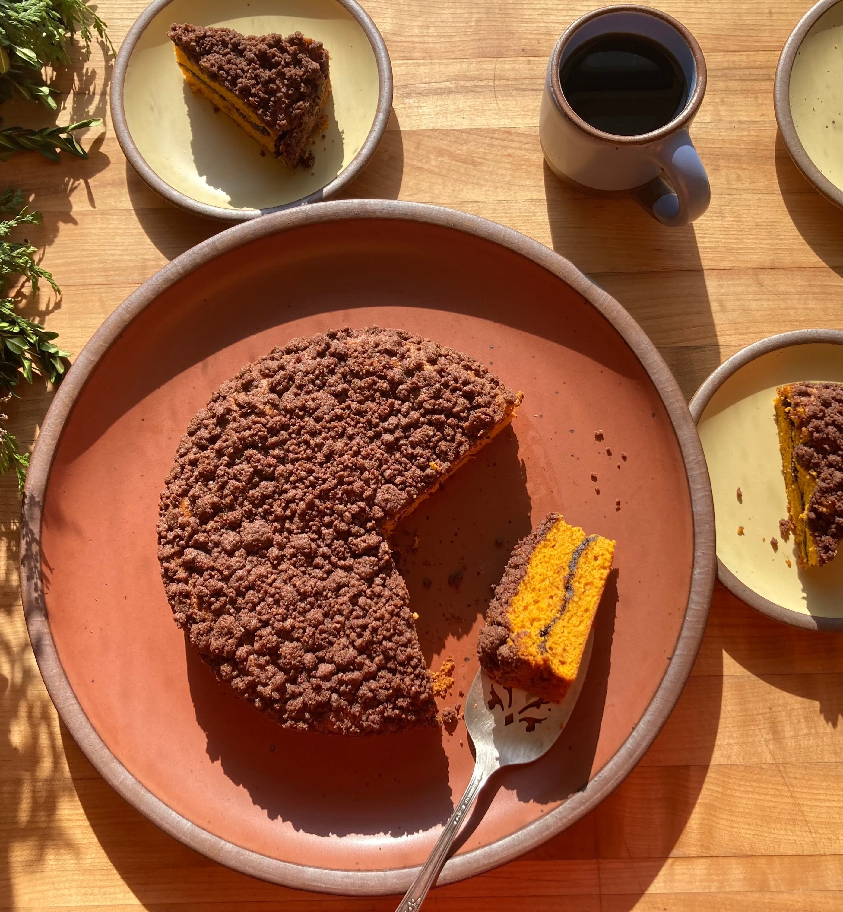 A butternut squash coffee cake sitting on a terracotta color plate with slices plated on small cake plates in a butter color.