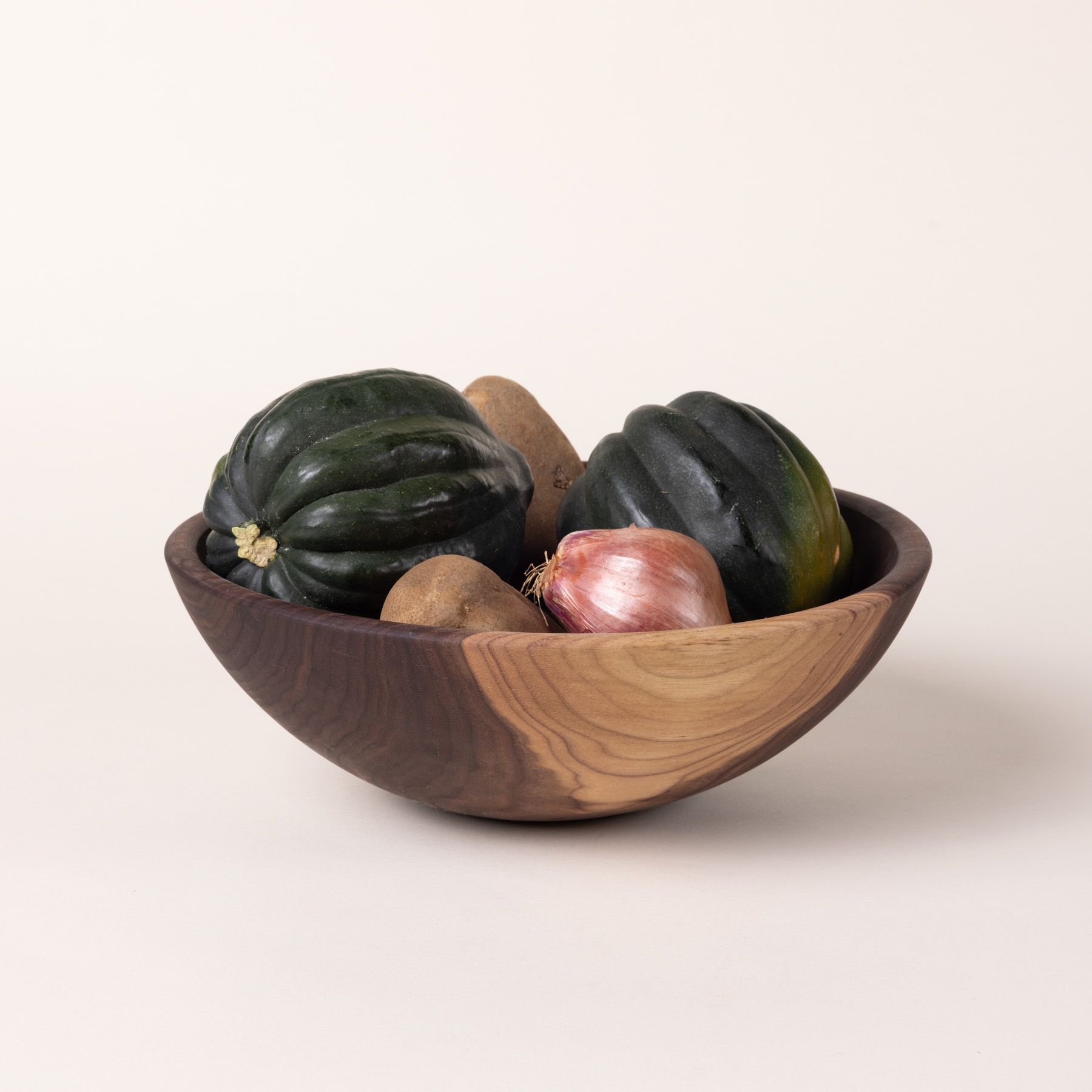 A large walnut wooden bowl filled with onion, potatoes, and squash