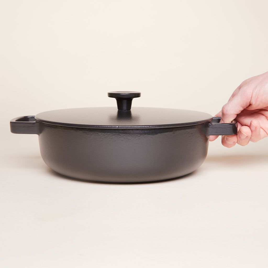 A hand touches a handle of a black cast iron pot that has a lid.