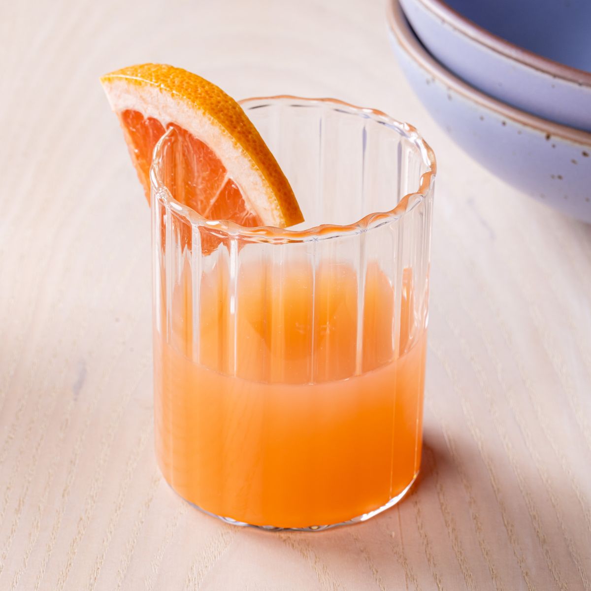 A short fluted glass tumbler filled with grapefruit juice and a slice of grapefruit