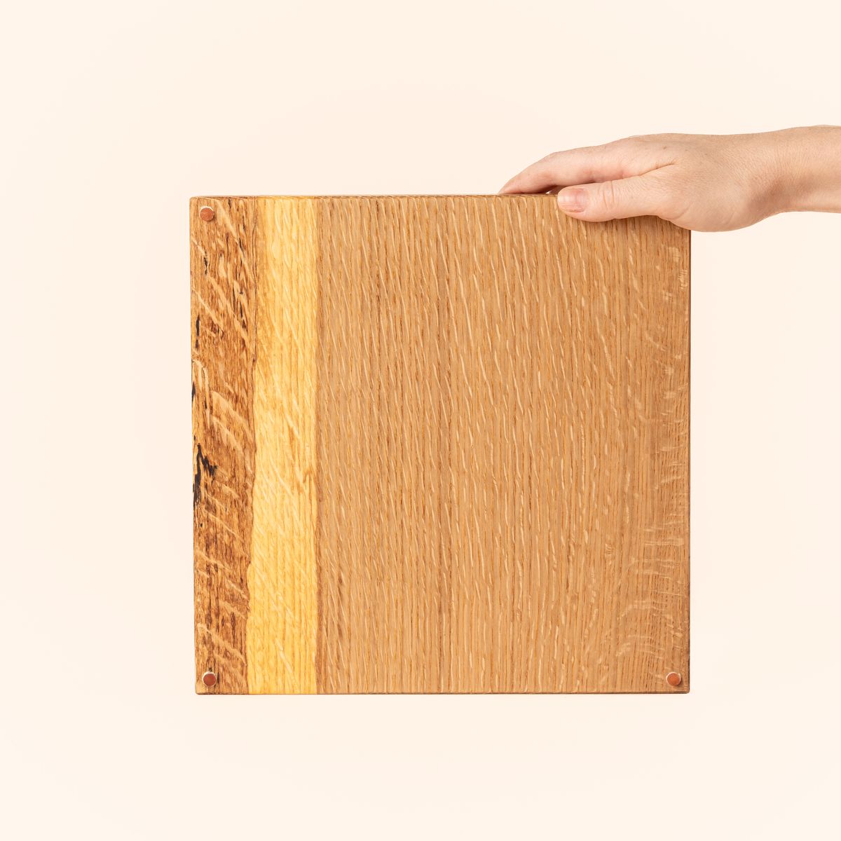 Hand holds up a thick rectangular cutting board made of light-colored wood