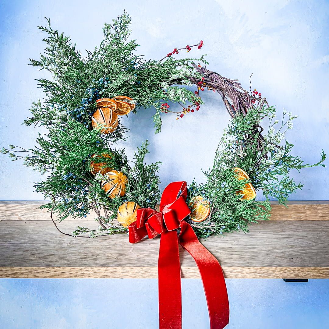 A handmade holiday wreath featuring some citrus slices and a large red bow sitting on a wooden shelf