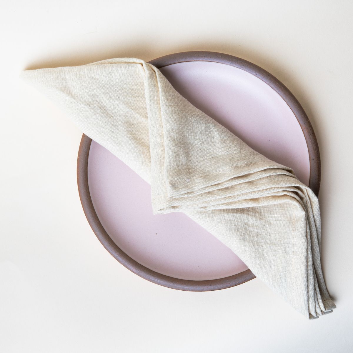 Folded linen napkin in a soft butter yellow on a soft light pink plate
