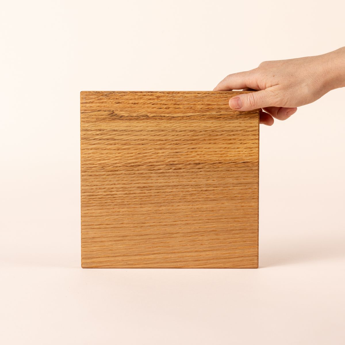 Hand holds up a thick rectangular cutting board made of light-colored wood