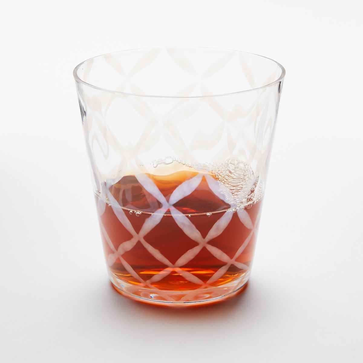A short clear glass with a delicate grid pattern, half filled with a drink