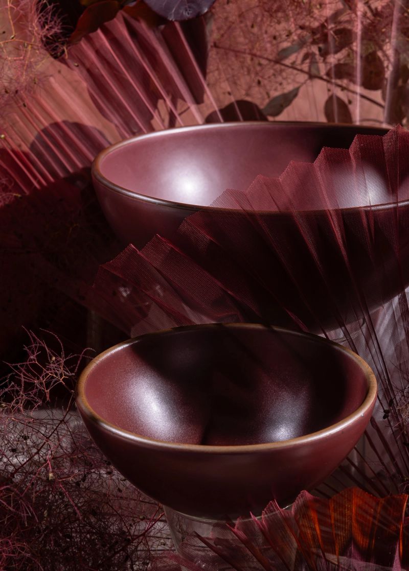 Ceramic bowls in a deep plum color are in a moody setting with abstract elements