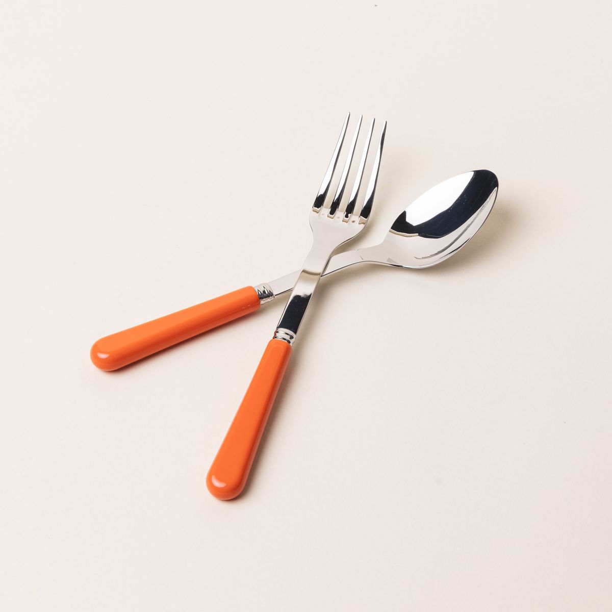 A serving size spoon and fork in a shiny steel with a bold orange handle