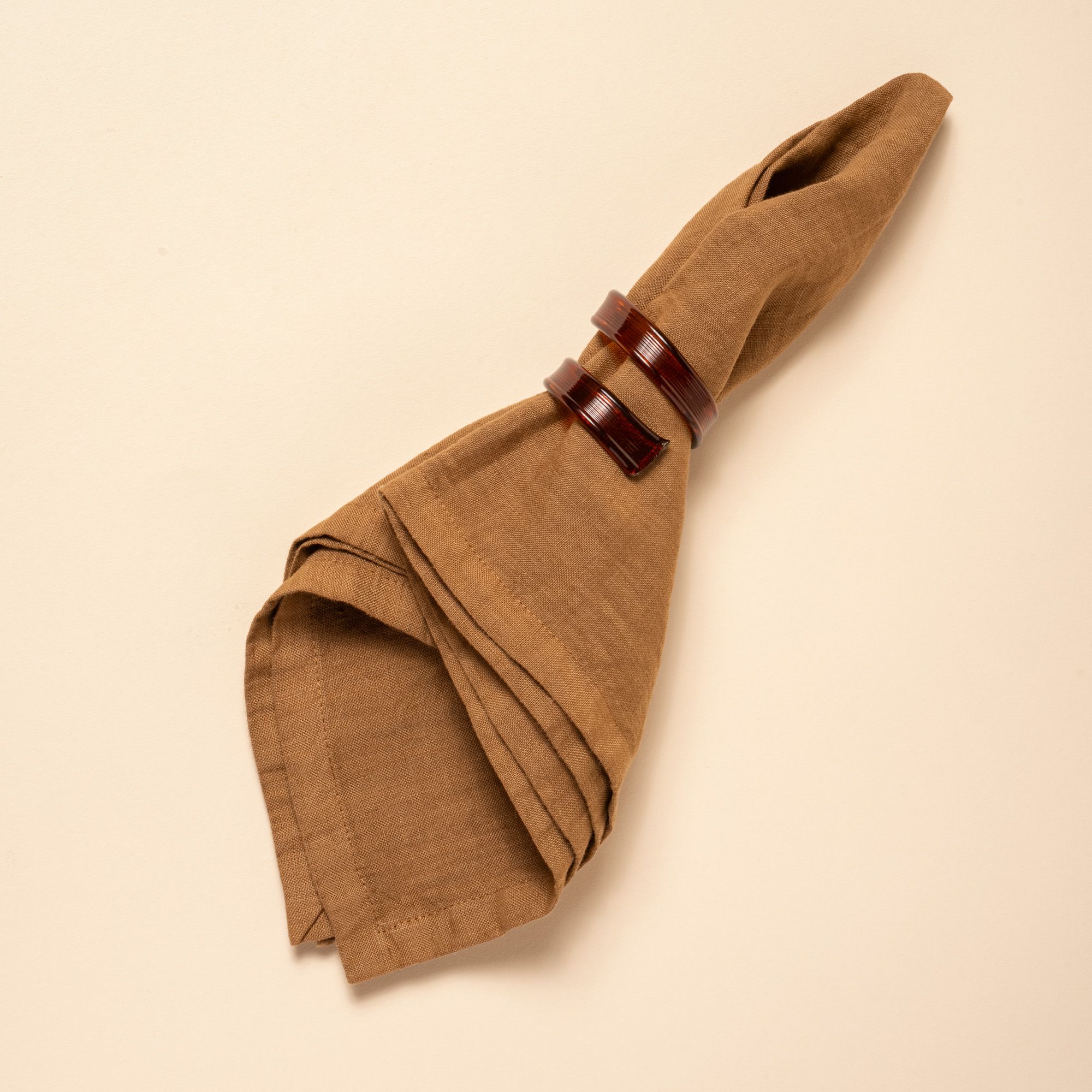 Brown linen napkin folded with curled recycle brown napkin rings, styled against a neutral background.