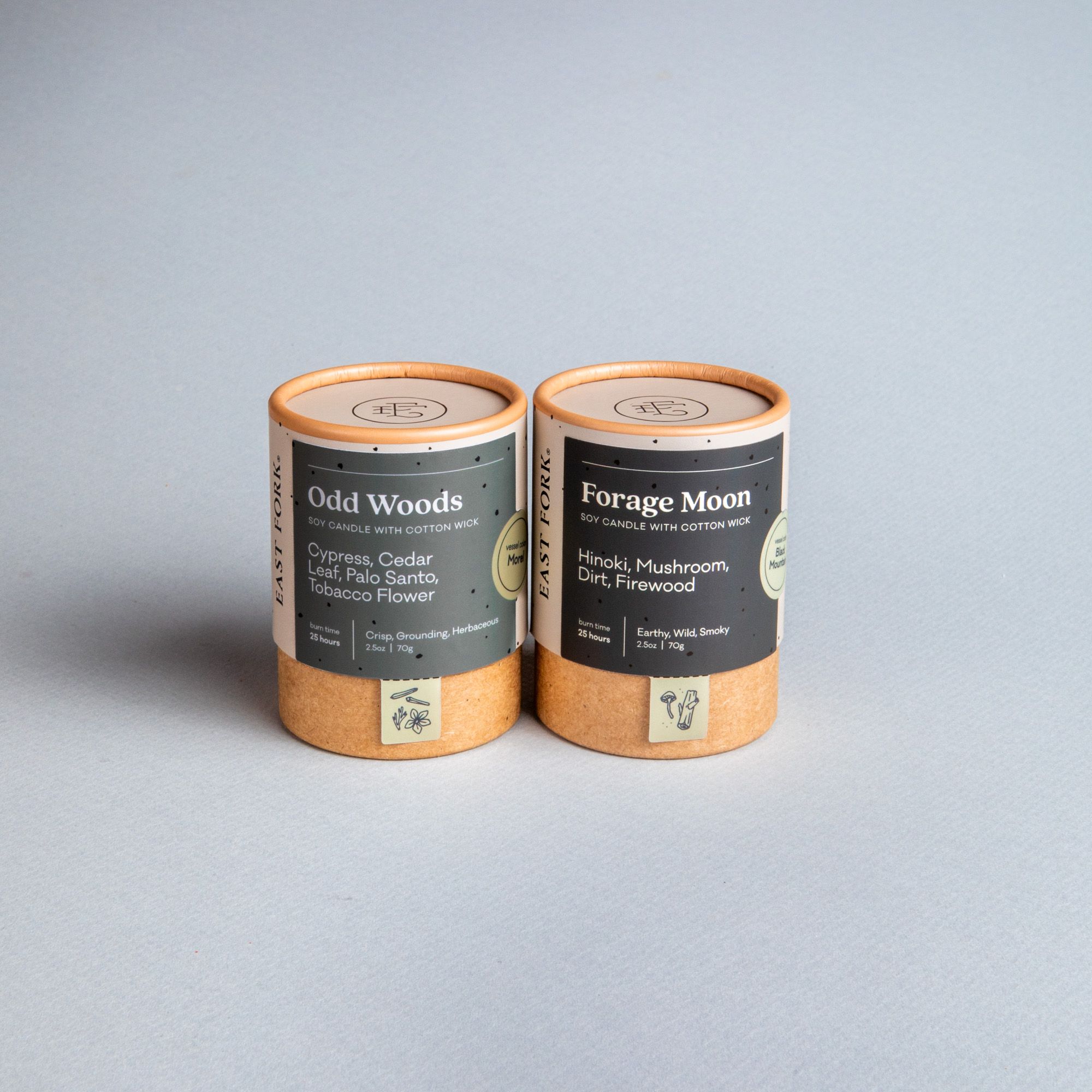 Two small cardboard packaging tubes with a candle inside each with branding on the outside that says 'Odd Woods' and 'Forage Moon'