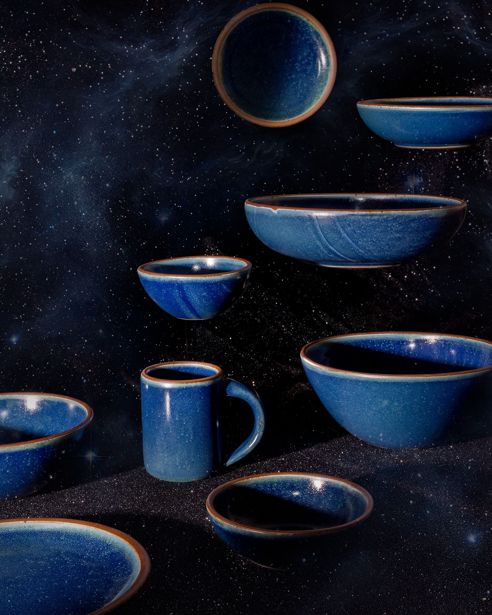 An artful arrangement of ceramic pottery in a dappled deep blue glaze floating up against a starry dark background.