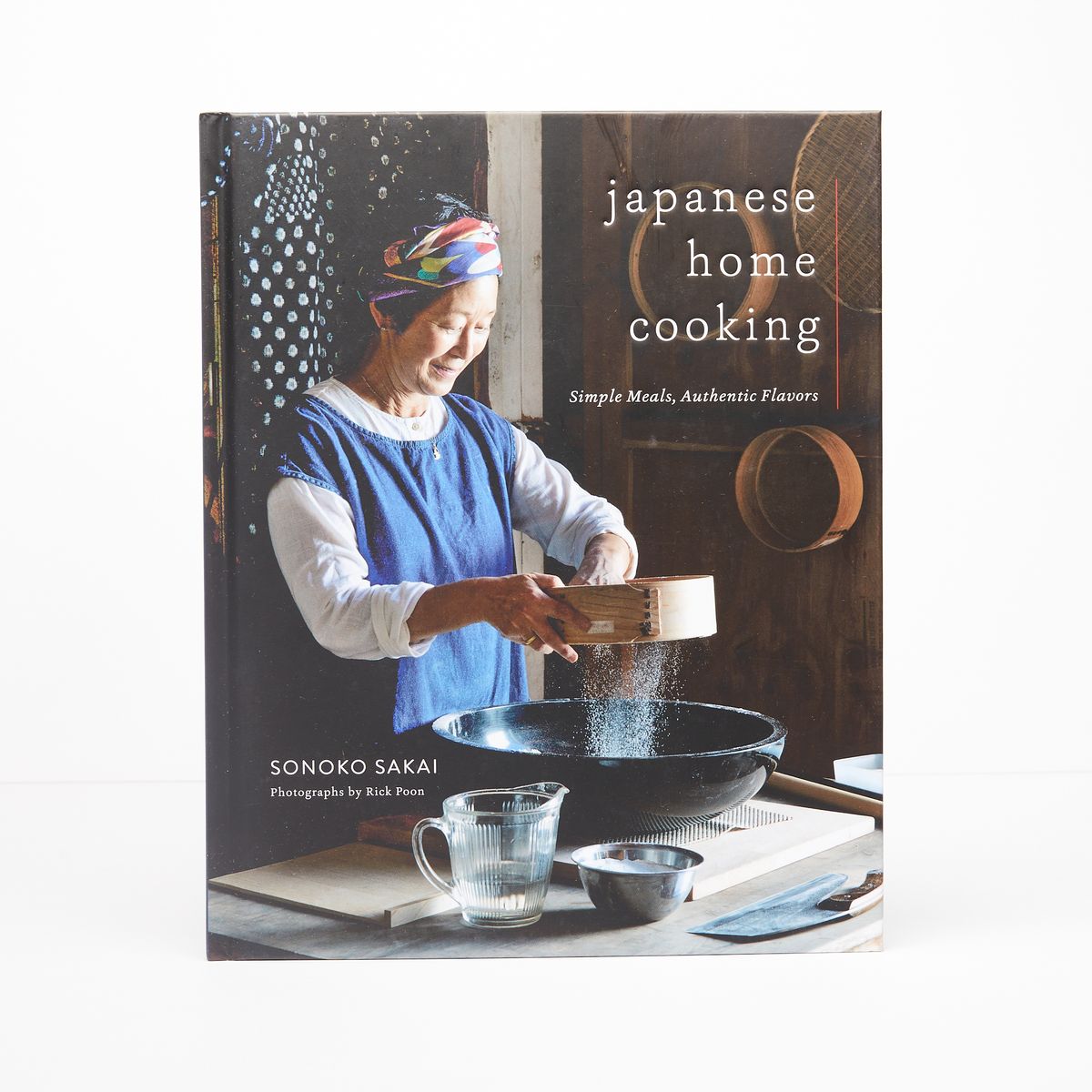 Cover of a cookbook with a photo of an older Japanese woman cooking with a title that reads "Japanese Home Cooking"