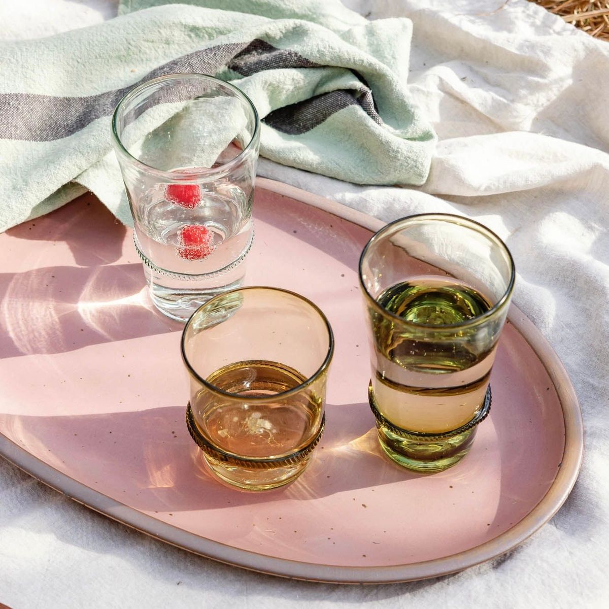 Three olive and clear glasses with a banded ring sit on a large oval platter in a dusty mauve pink outside.