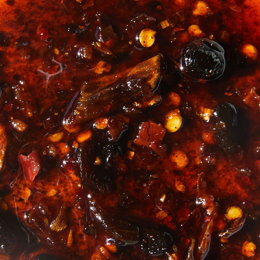 Close-up of chili crisp, a thick liquid in shades of red with spices that are red or yellow