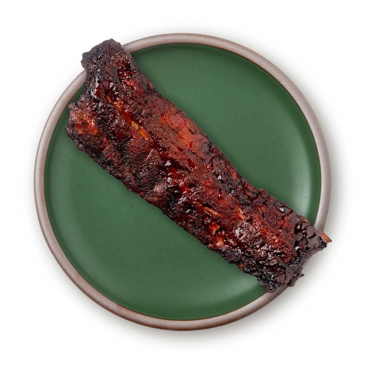 A rack of ribs on a large ceramic platter in a deep, verdant green color featuring iron speckles and an unglazed rim