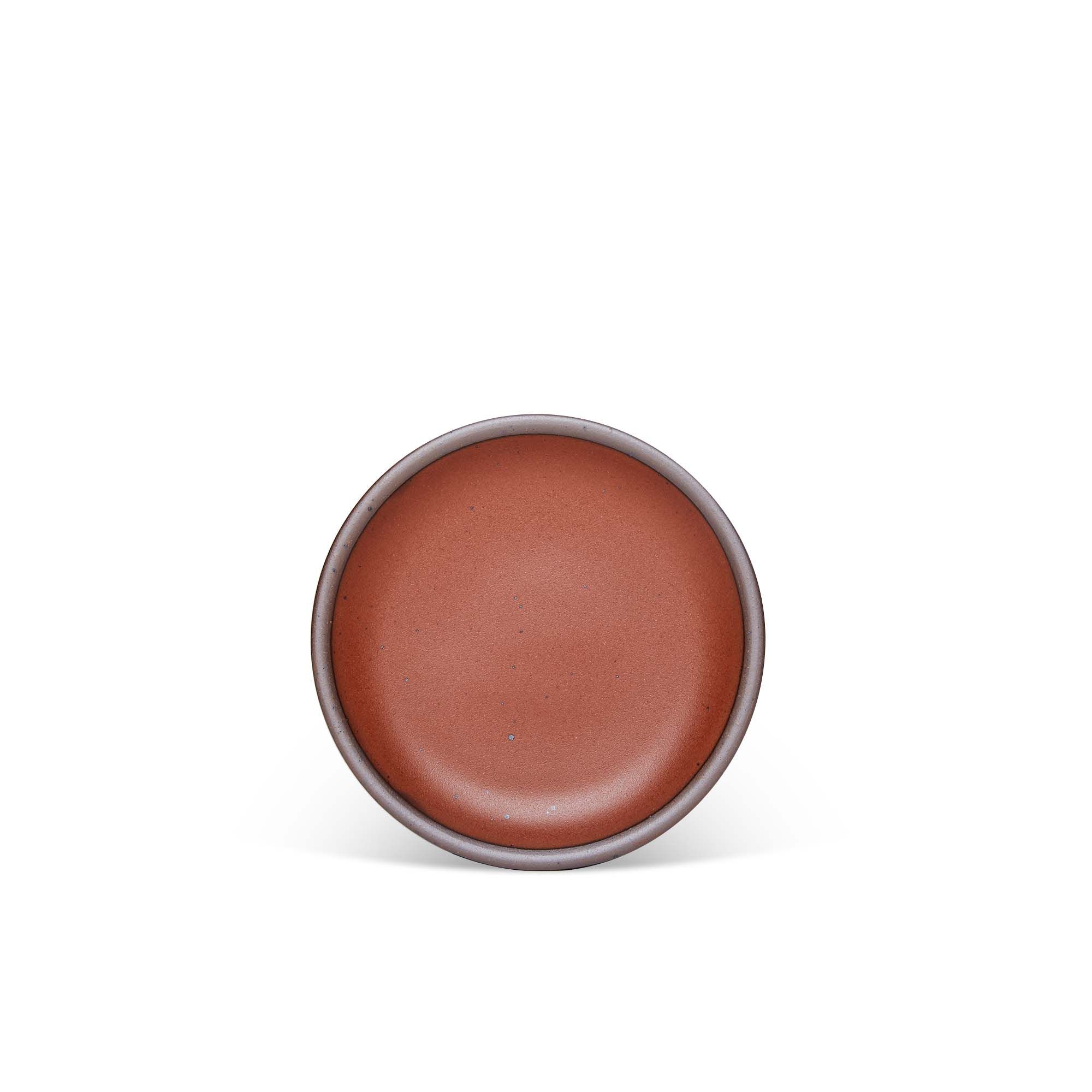 A dessert sized ceramic plate in a cool burnt terracotta color featuring iron speckles and an unglazed rim.