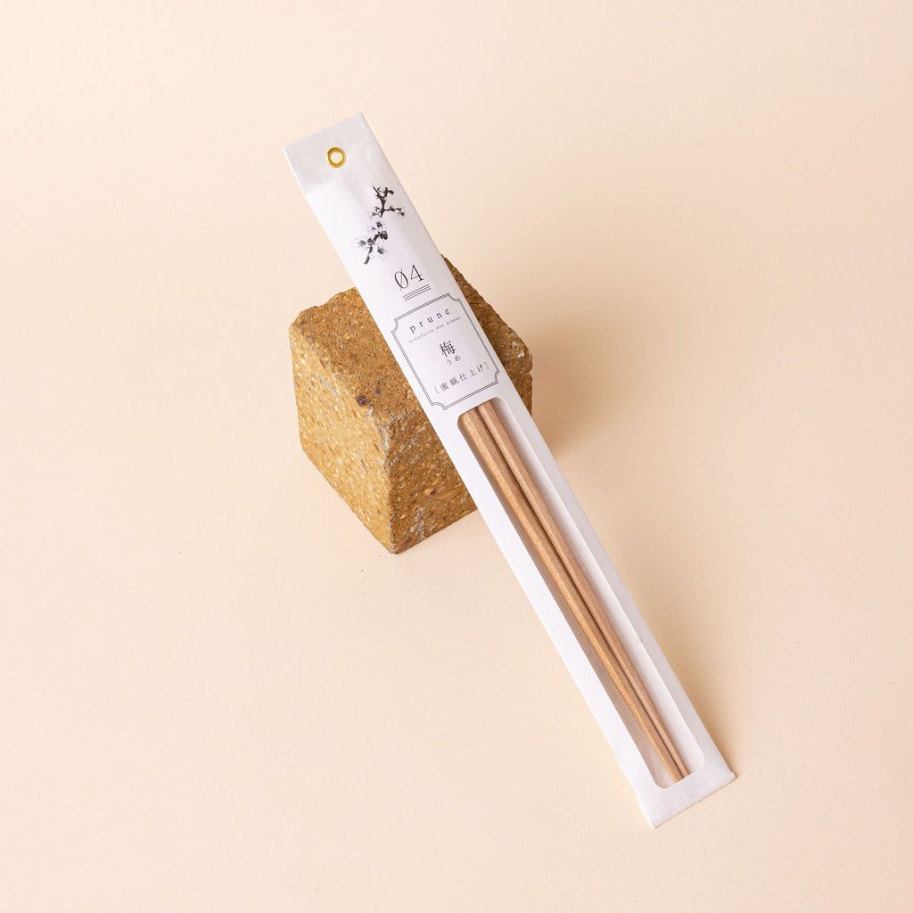 Simple pair of light wood chopsticks packaged in thin paper packaging leaning against a square brick
