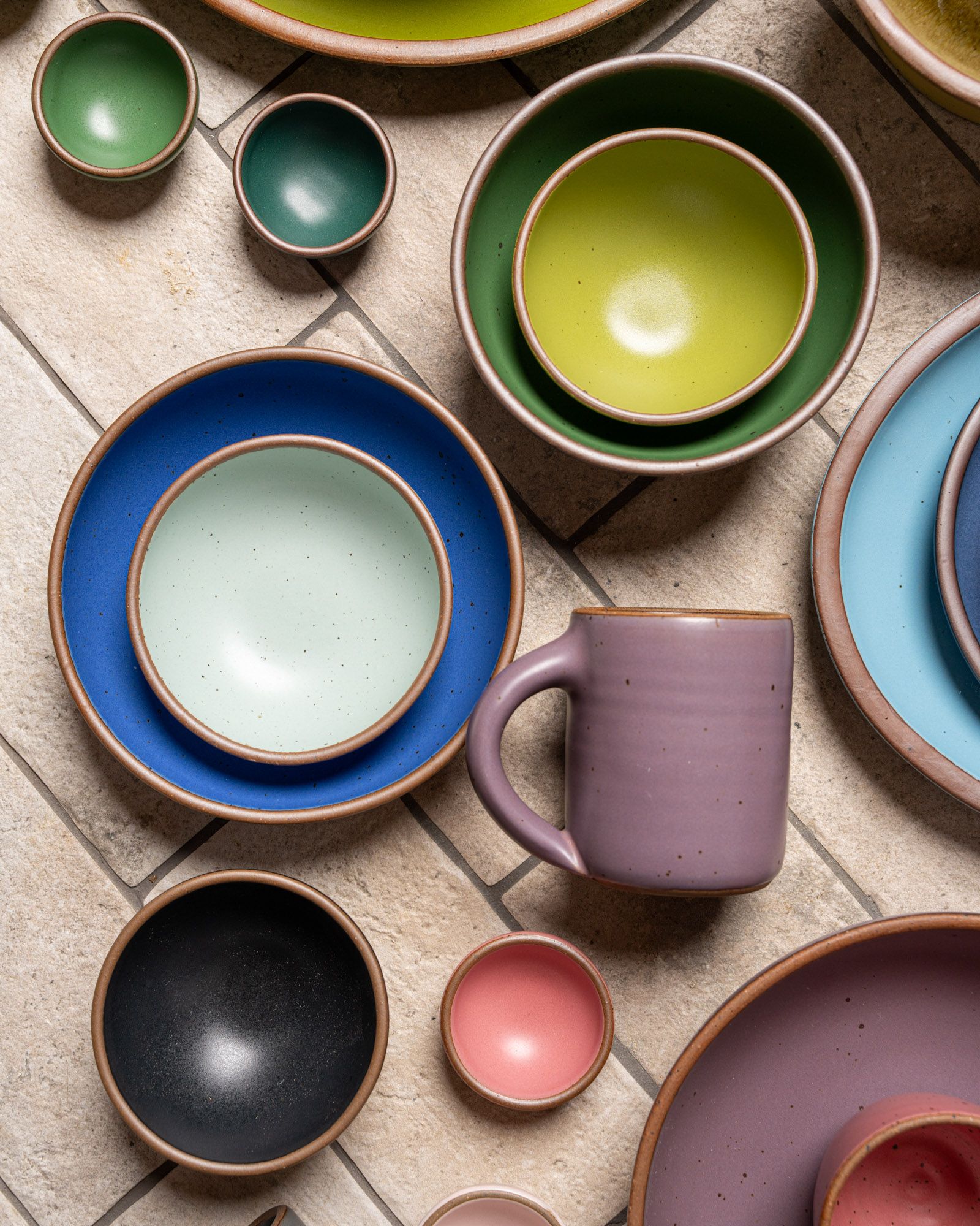 An artful arrangement of ceramic bowls and a mug, all in different colors of the rainbow.
