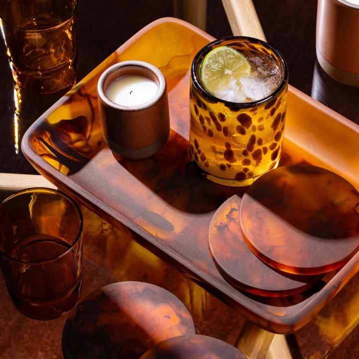 A tortoiseshell rectangular tray with tortoiseshell circular coasters, a cocktail, and a small candle.