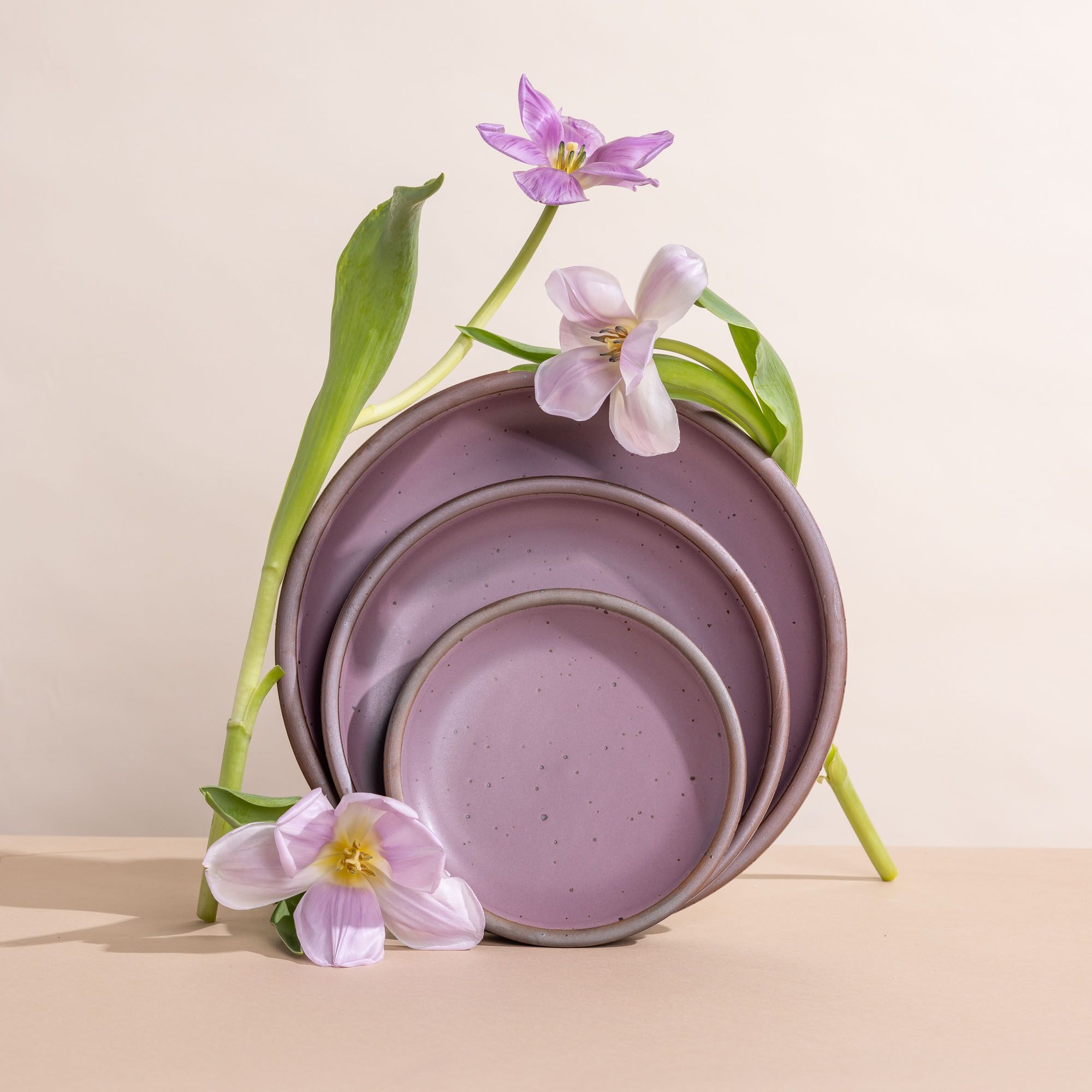 A trio of cake, side, and dinner plates propped up in a soft, mauve purple color with purple flower stems.