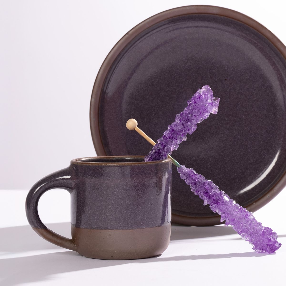 A small ceramic mug and plate in a glossy purple color styled with purple rock candy