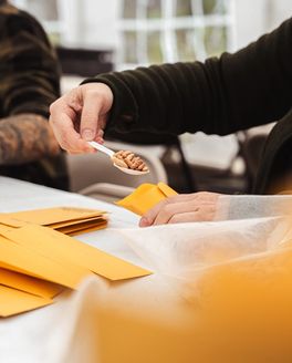A hand scoops seeds into a manila envelope.