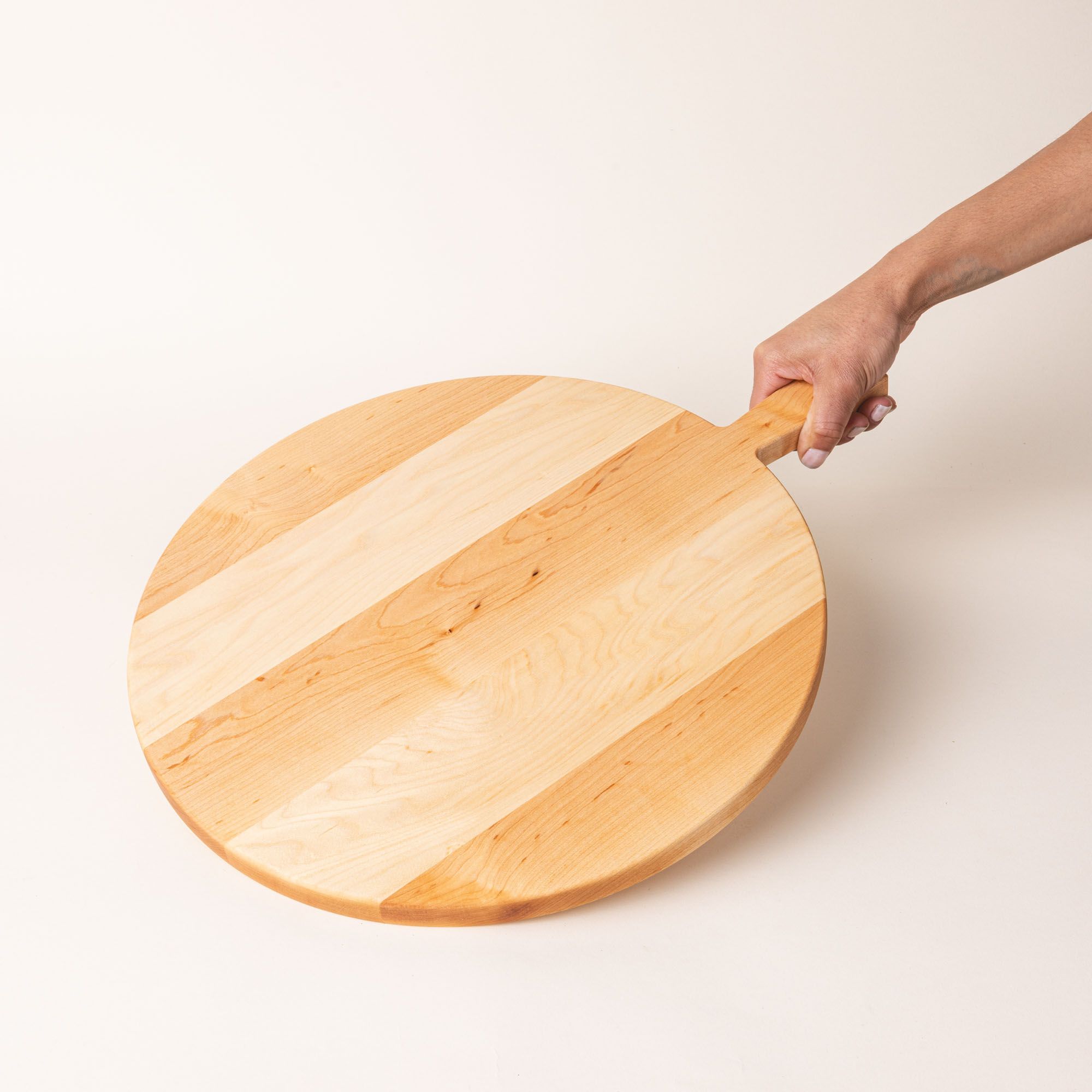 A round wooden serving board with a short rectangular handle with a hole for hanging