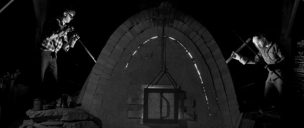 A black and white image of two men investigating the sides of a large wood kiln