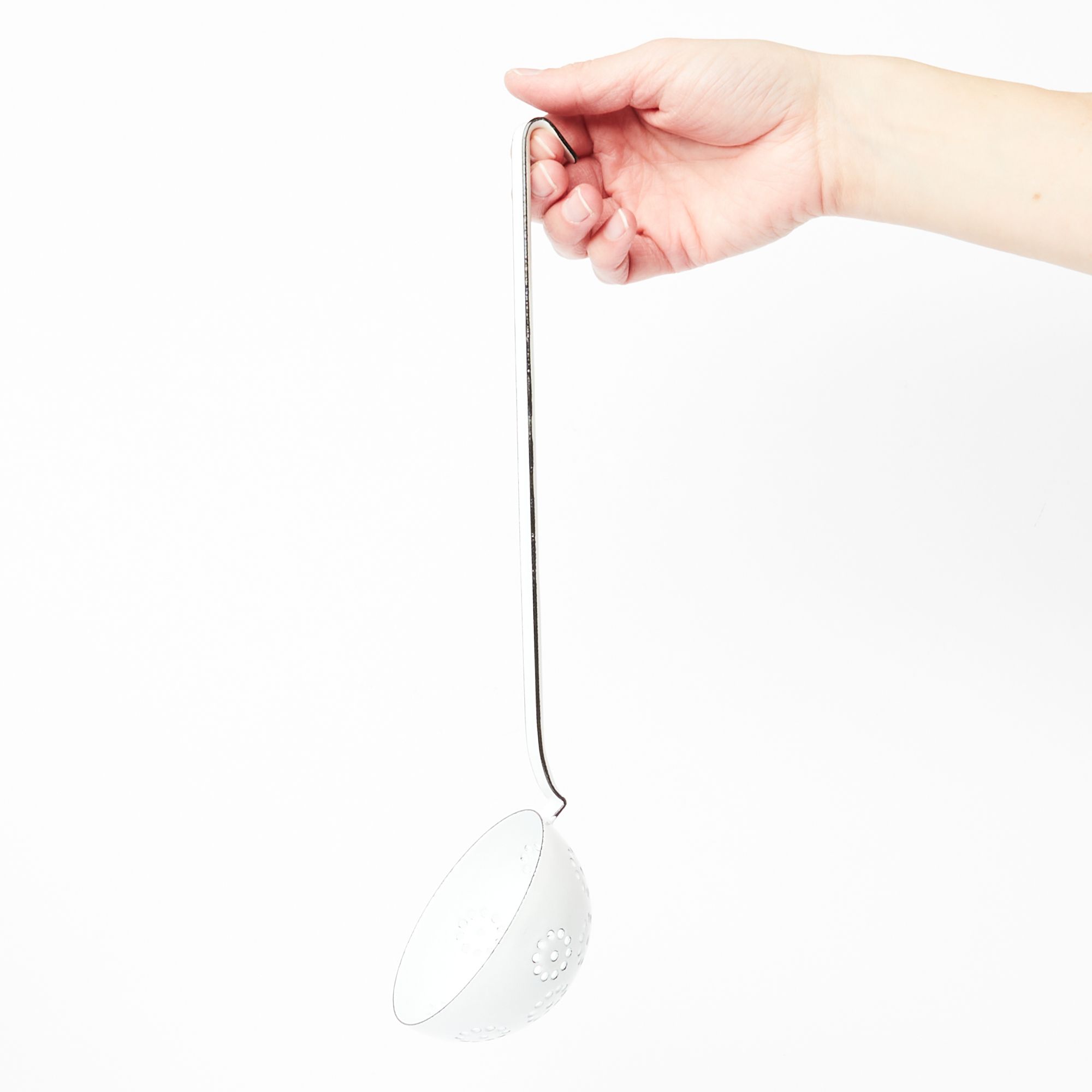 A hand holding a white enamel ladle with little slotted holes inside the ladle scoop.