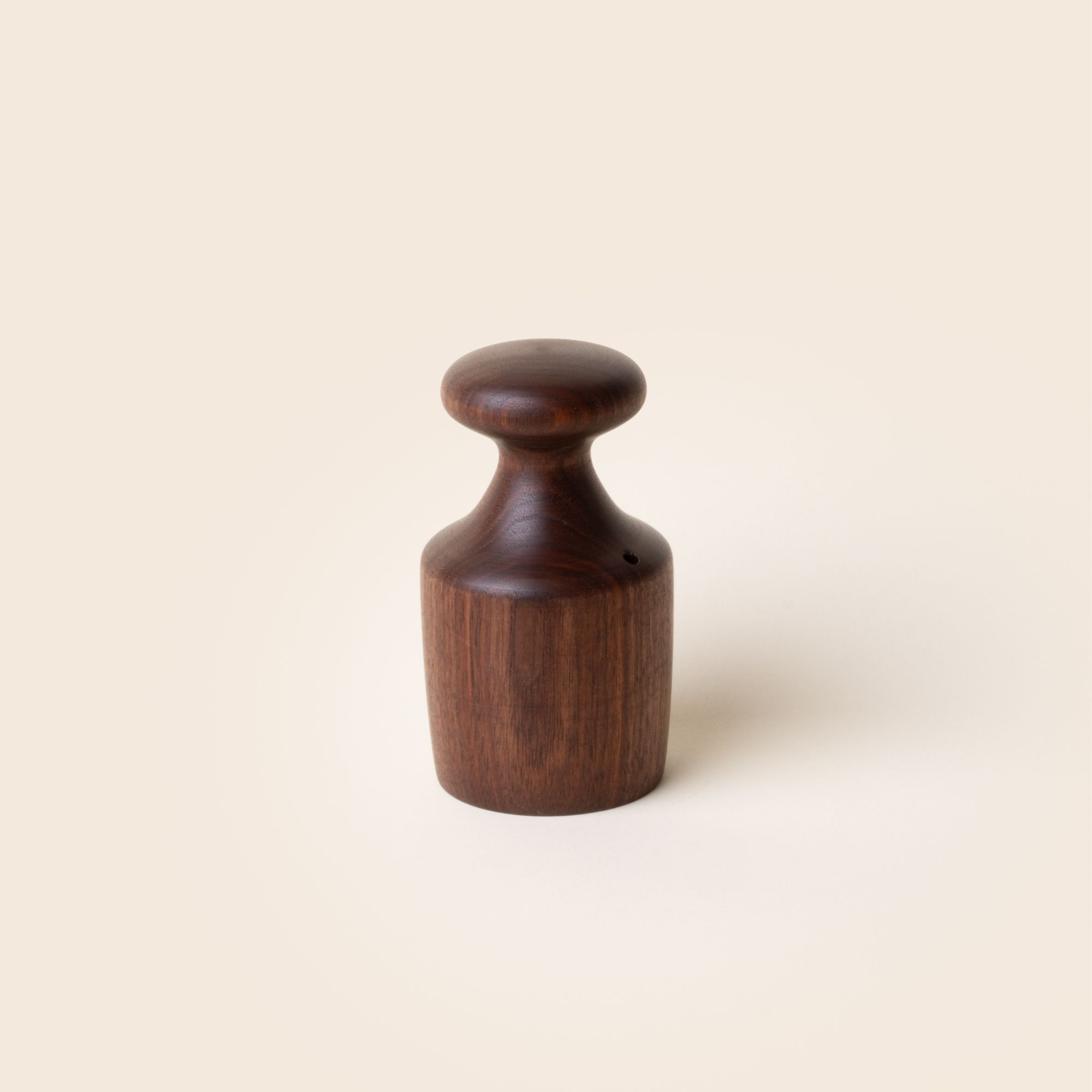 A turned black walnut biscuit cutter with a knob at the top of a cylindrical black