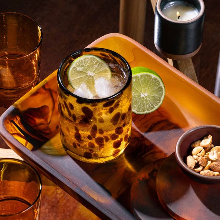 A tortoiseshell drinking glass filled with a drink and sitting on a tortoiseshell tray with coasters