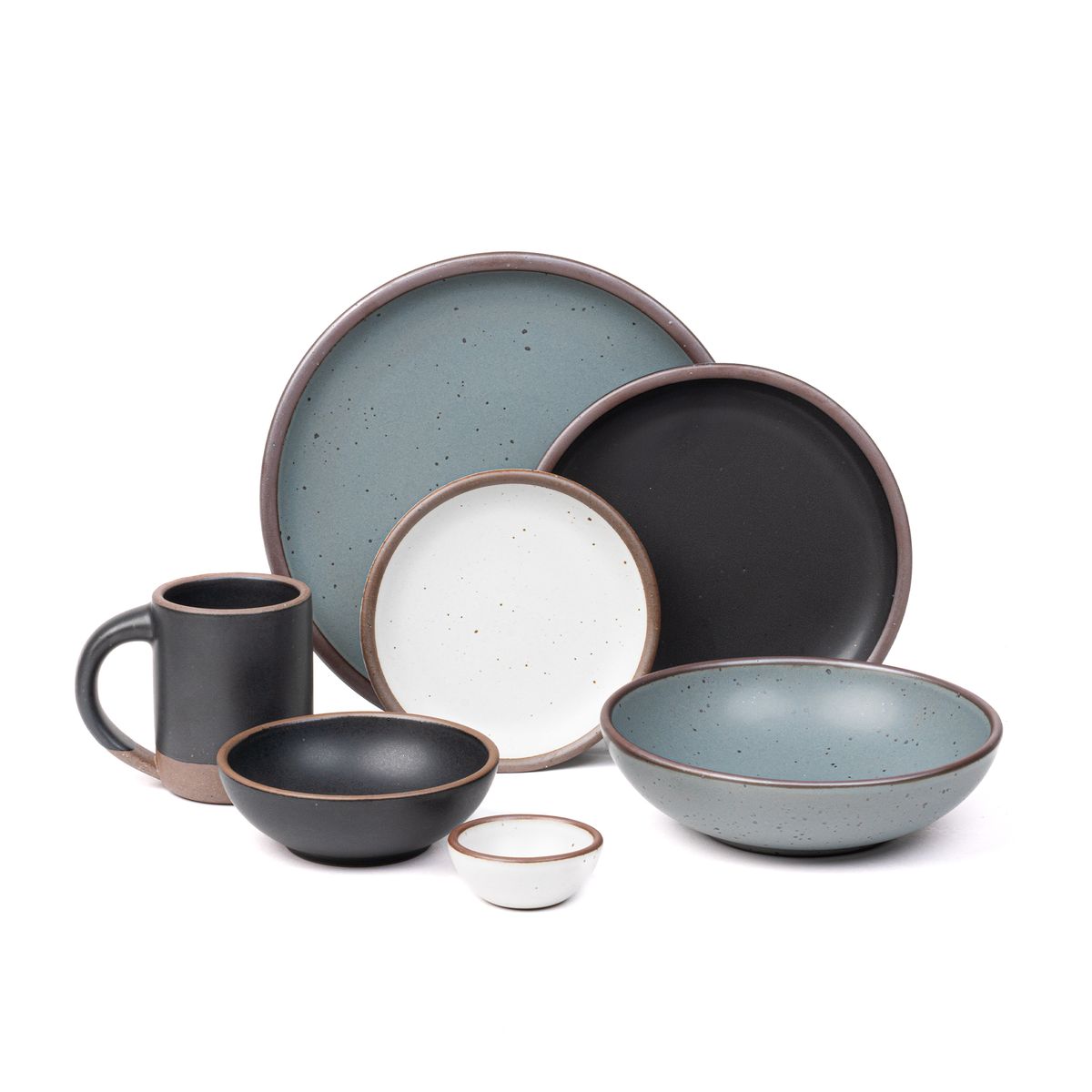 The Mug, side plate, and breakfast bowl in graphite black, the bitty bowl and cake plate in cool white, the everyday bowl and dinner plate in a blue-grey color.