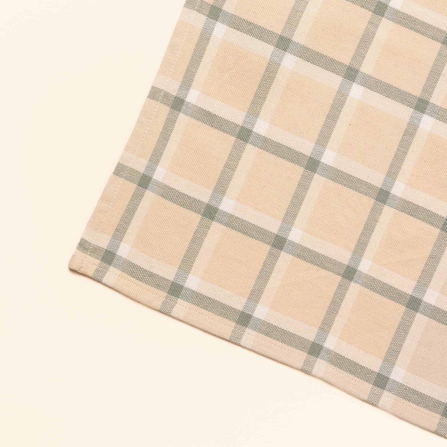 A close up of a corner of a gingham rectangular placemat in cream, off-white, and sage green colors