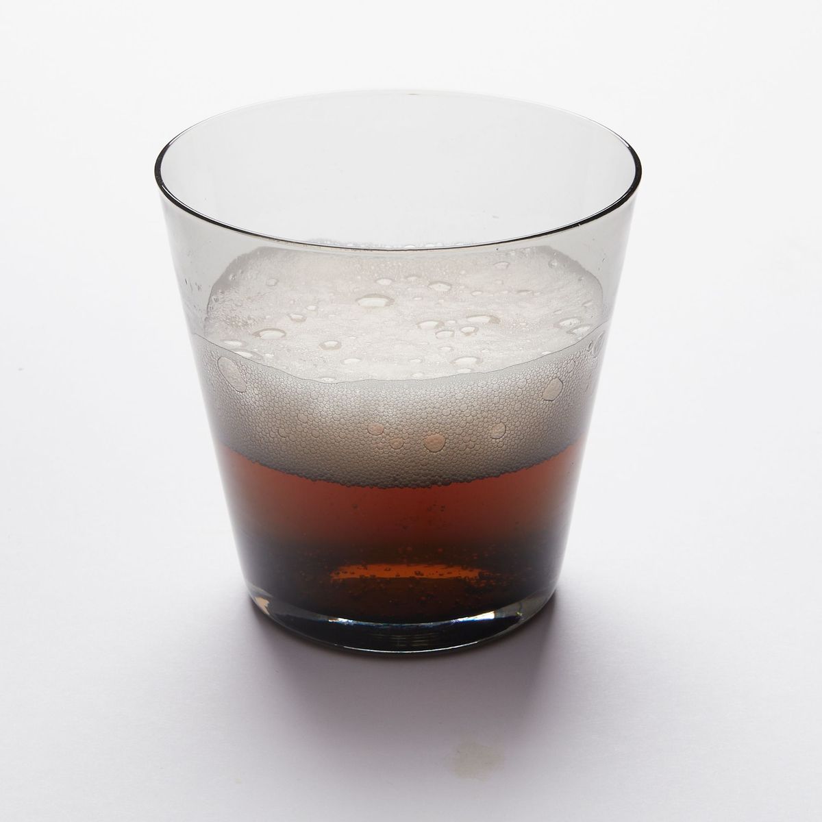 A short drinking glass made of black colored glass, half filled with an amber drink