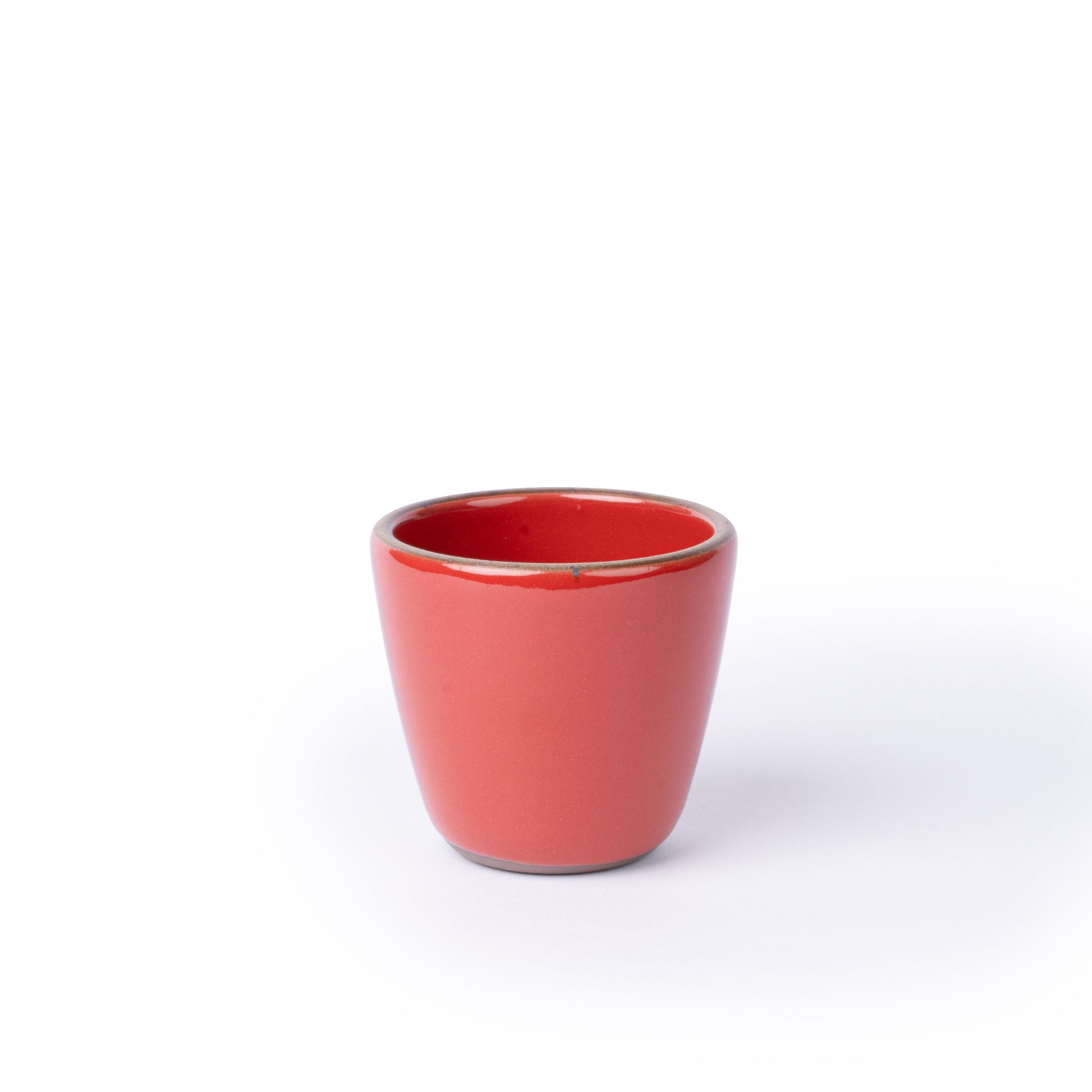 A short cup that tapers out to get wider at the top in a glossy red color featuring iron speckles