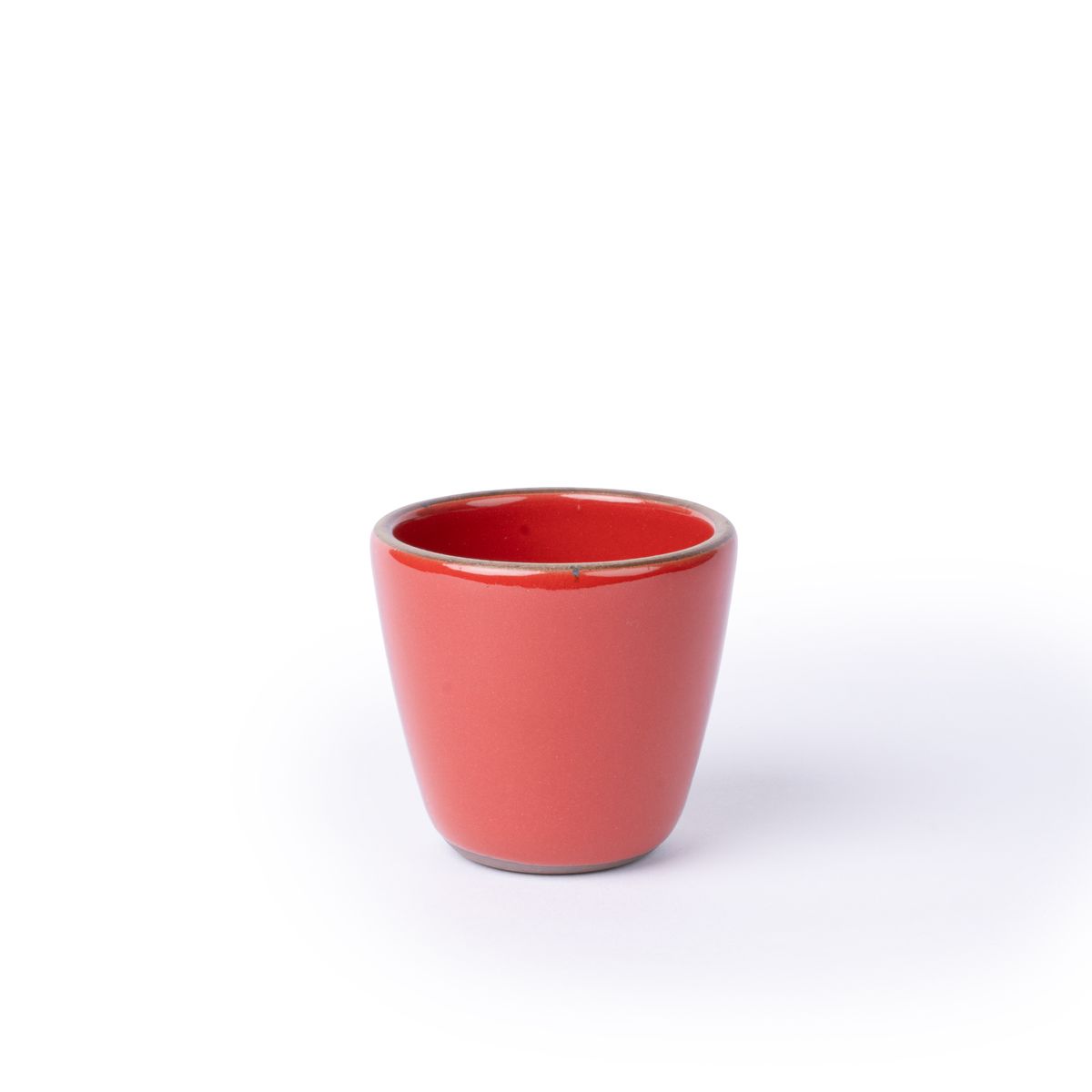 A short cup that tapers out to get wider at the top in a glossy red color featuring iron speckles