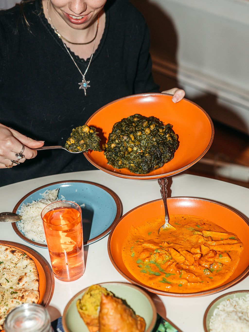 A dinner party table filled with various ceramic plates and bowls in bold colors, drinking glasses, and glimpses of people eating and talking.