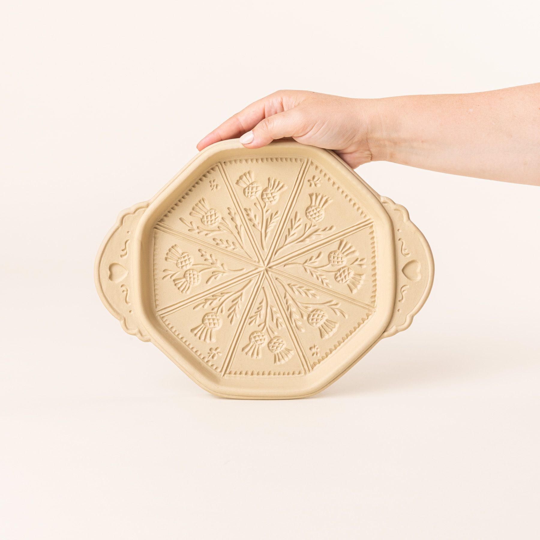 A hand holds up a shortbread pan with a thistle flower design on the bottom