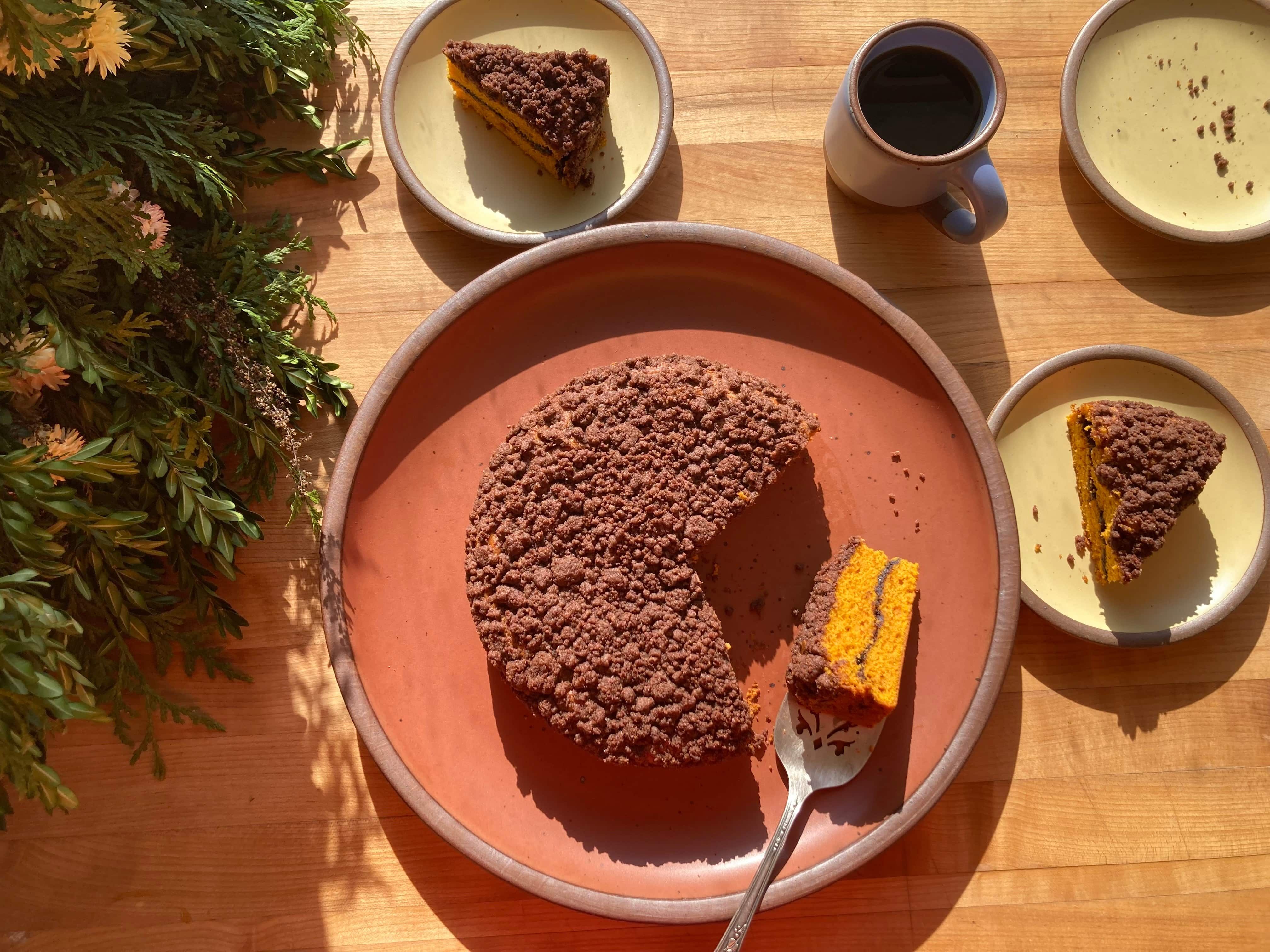 A butternut coffee cake sitting on a terracotta color plate with slices plated on small cake plates in a butter color.