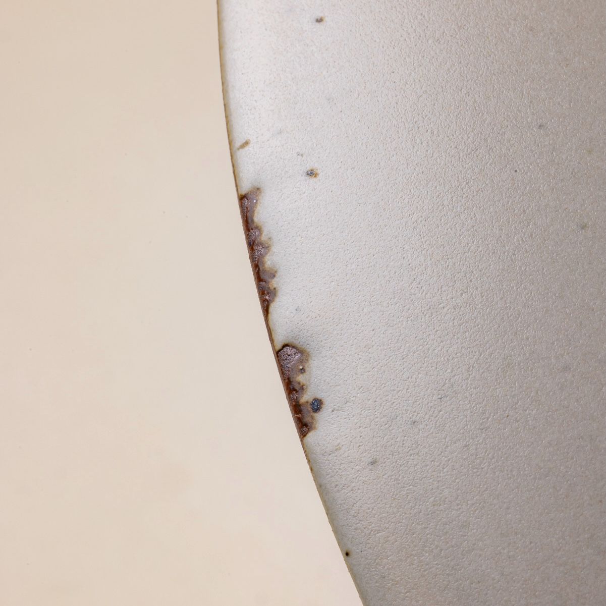 The edge of a ceramic bowl in a cool white color shows scuffs where the glaze was rubbed off, revealing unglazed clay.
