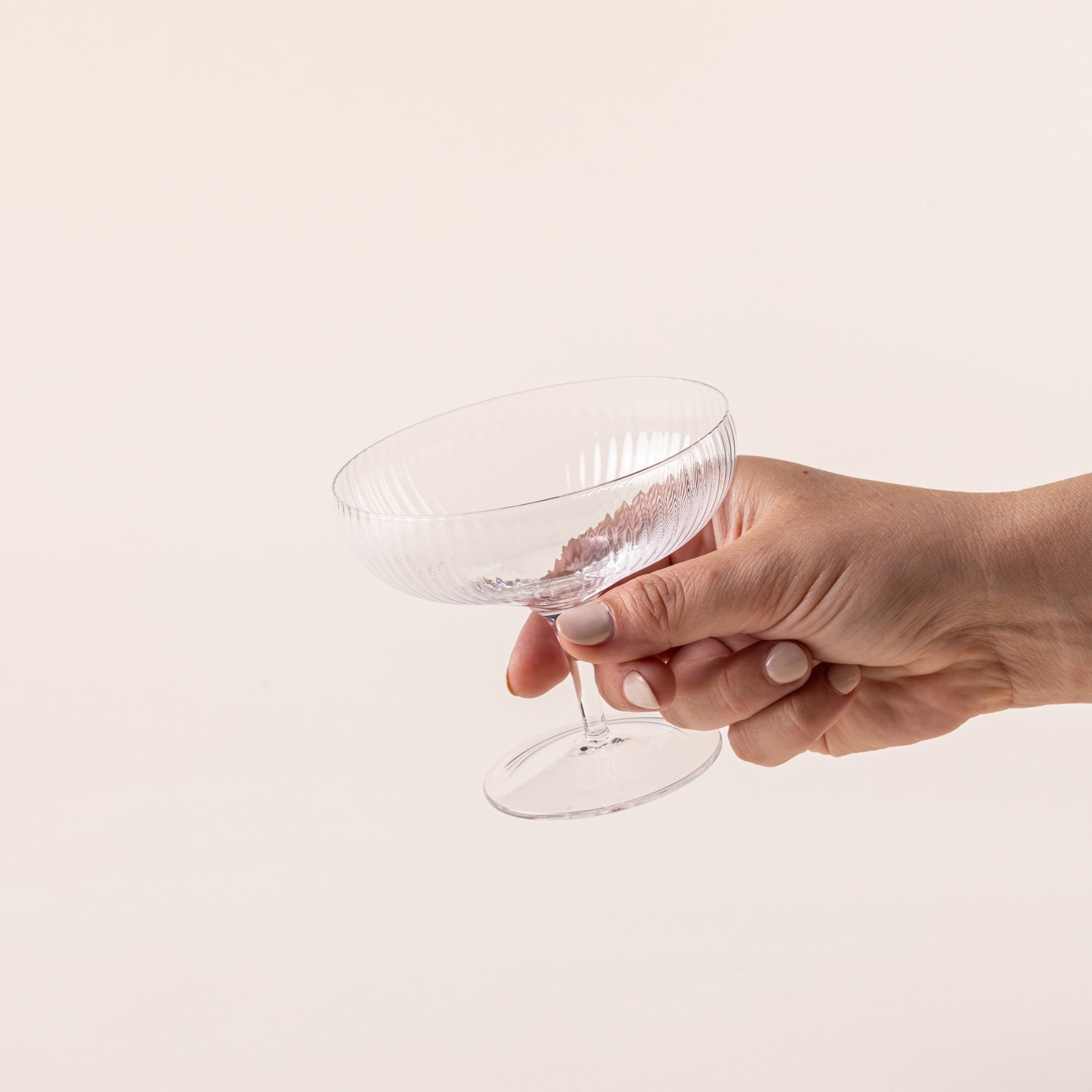 A hand holds a delicate ribbed short coupe glass in the traditional style